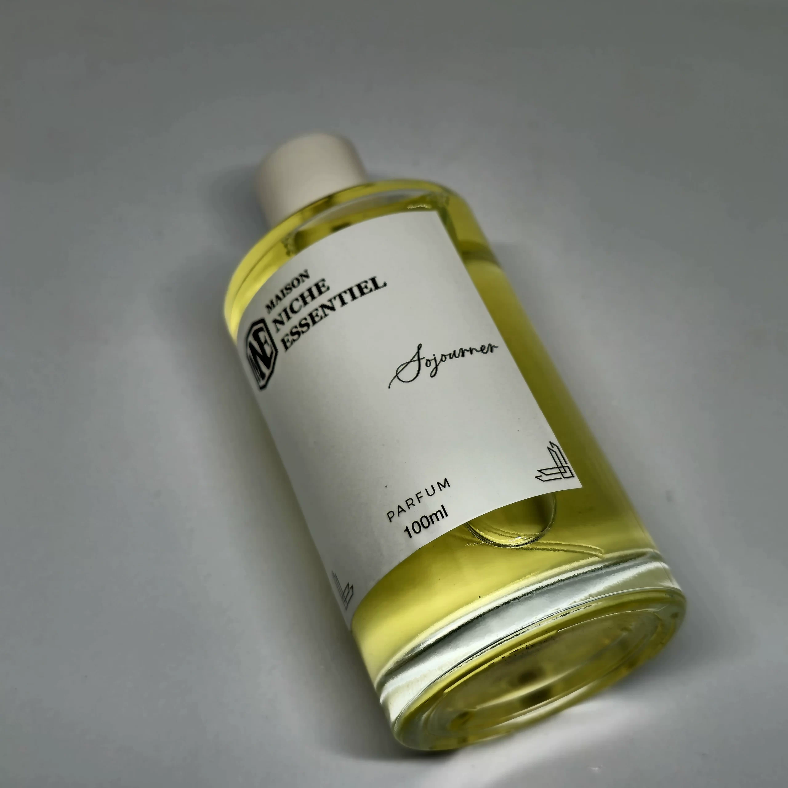 Transparent bottle of Maison Niche Essentiel perfume with a white label and yellow liquid inside.